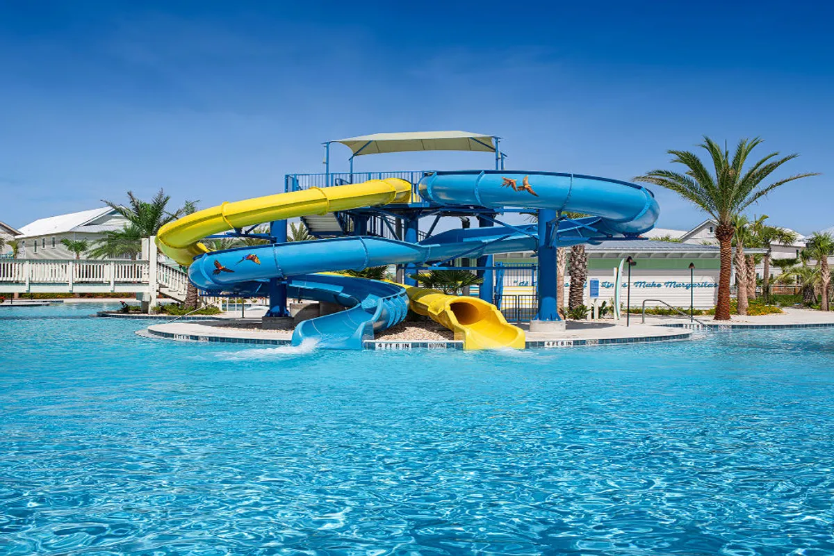 A lively exterior shot featuring a large swimming pool with vibrant water slides twisting between palm trees. The pool area is bustling with families and children enjoying thrilling water activities, perfectly capturing the essence of all-ages resort fun.