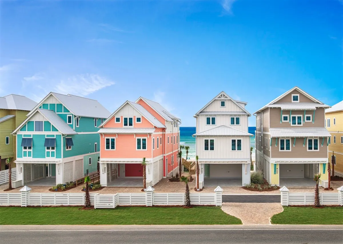 This image features a row of colorful beachfront houses in pastel shades, each with balconies overlooking the Gulf. A private dune walkover connects the villas directly to the sugar-white sandy beach, and the turquoise ocean shimmers in the background. White picket fences and well-maintained landscaping contribute to a vibrant, family-friendly atmosphere.