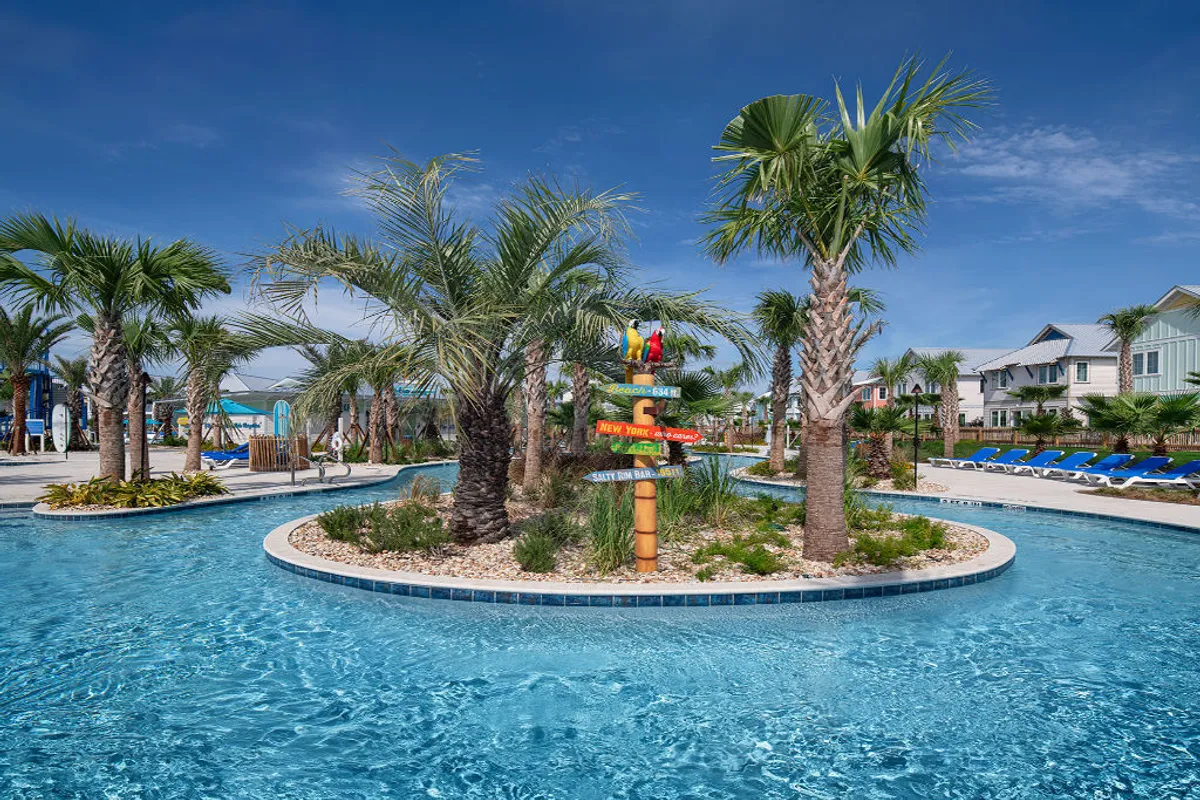 A vibrant shot of the resort’s lazy river curving through lush, tropical landscaping, with blue lounge chairs lining the poolside and a whimsical signpost with parrots adding a playful touch. The atmosphere is cheerful and relaxed, with guests floating or sunbathing.